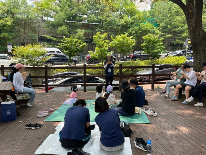 강사가 앞에 서있고 강사를 바라보며 앉은 사람들이 설명을 듣는다